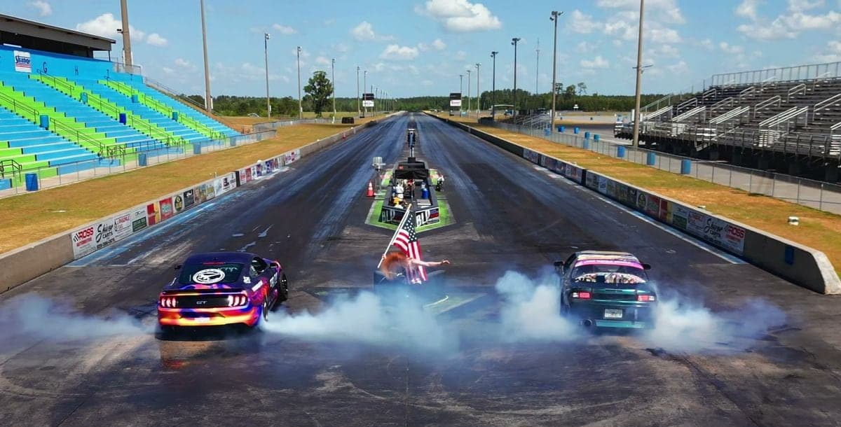 Three cars doing side-by-side burnouts on the drag strip in front of the grandstands